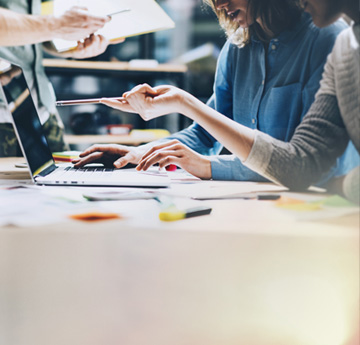Two people looking at a laptop together. One is pointing at the screen with a pen.