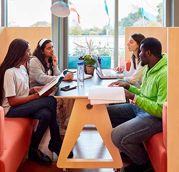 Four students chatting at a table within Harbwr Fulton on Swansea University's Singleton Campus